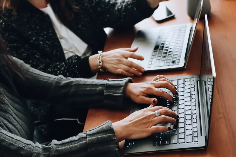 two women sitting at a table working on laptops